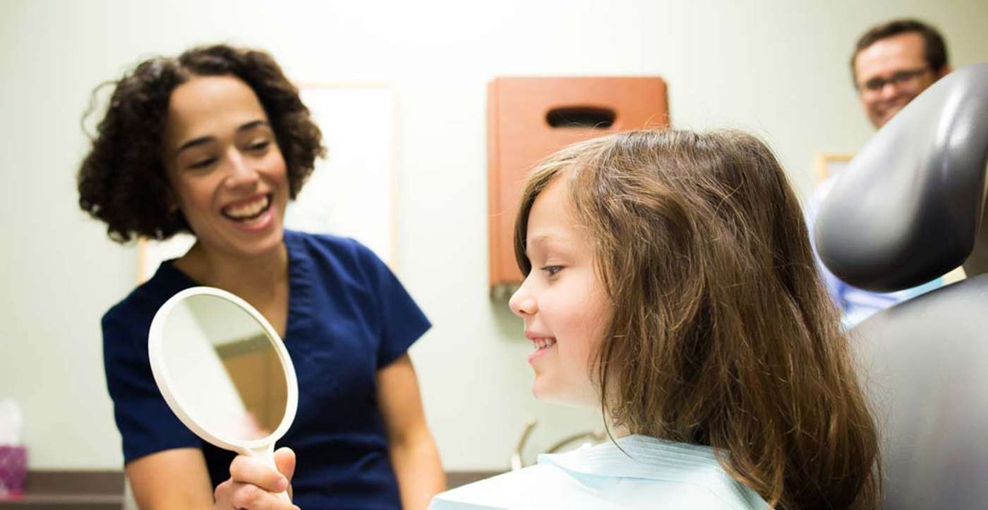 Young girl patient smiling into mirror held by dental hygienist