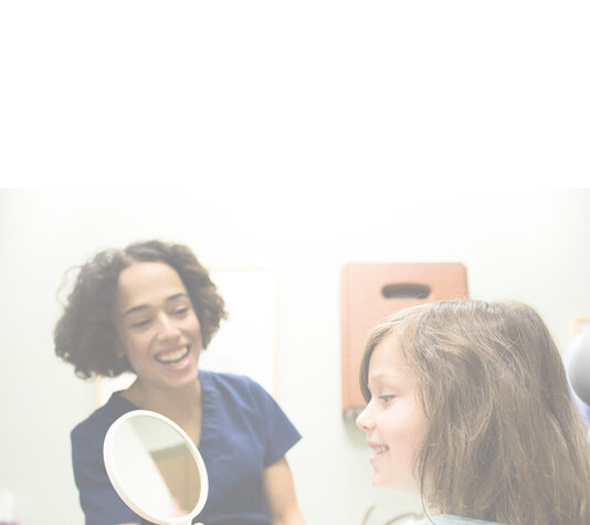Young girl patient smiling into mirror held by dental hygienist